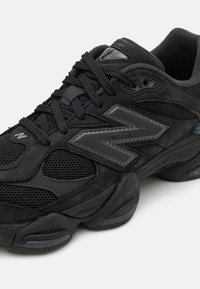 Black athletic shoe featuring a mix of suede and mesh textures, prominent 'N' logo, and padded collar with black laces.
