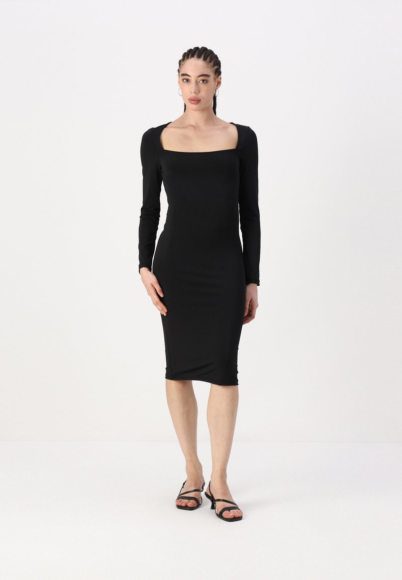 Ilga suknelė juoda, prigludusi prie kūno, su kvadratiniu iškirpimu, pagaminta iš lygaus audinio, iki kelių, su šoninėmis raukšlėmis. Suporuota su juodais strapiniais sandalais.