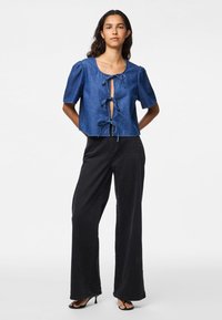 Τζιν κοντό τοπ με φουσκωτά μανίκια, λεπτομέρεια με κόμπο μπροστά και βαθύ V-ντεκολτέ. Συνδυάζεται με ψηλόμεσα μαύρα παντελόνια σε ίσια γραμμή και τακούνια.