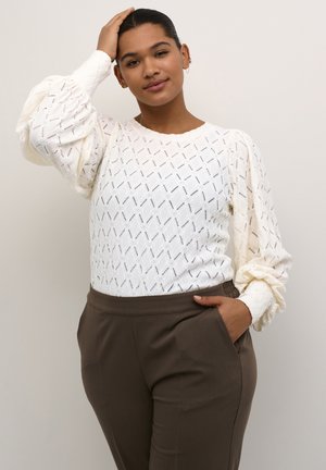 White textured sweater with diamond patterns and billowy sleeves. Paired with brown tailored trousers. Clean, modern design.
