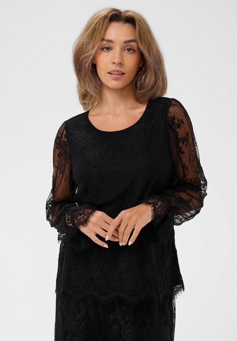 Czarna koronkowa bluzka z długimi przezroczystymi rękawami, ozdobiona floralnymi wzorami i okrągłym dekoltem. Miękka tekstura, warstwowy fason i falbaniasty dół.