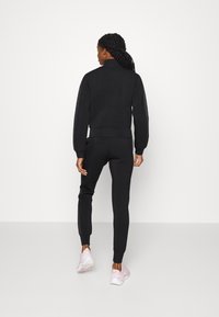 Svart sweatshirt og matchende bukser laget av myk stoff. Sweatshirten har høy krage og ribbede mansjetter; buksene har ankelsmansjetter.