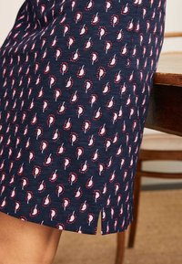 Mörkblå tygkjol med ett upprepande mönster av ljusrosa och röda paisleymotiv, med en sidoremsa för rörelse och textur.