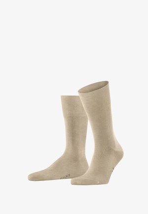 Chaussettes en coton beige avec texture côtelée, longueur mi-mollet et pointe renforcée. Nom de marque "FALKE" imprimé sur la semelle.