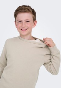 Beige sweatshirt met een ronde halslijn en geribbelde manchetten. De stof lijkt zacht en textuur te hebben, met een losse pasvorm en een lichte slouch op de schouder.