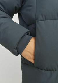 Dark padded jacket featuring a soft texture, side pocket, elasticized cuffs, and a smooth finish. The color is a deep navy blue.