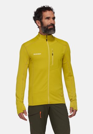 Veste en polaire jaune avec un col montant, poche poitrine zippée et trous pour les pouces. Présente un motif texturé et des coutures contrastantes.
