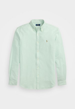 Svetlo zelena prugasta srajca z dolgimi rokavi, ovratnikom na gumbe in majhnim vezenim logotipom na levi strani.