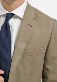 Beige skräddarsydd kavaj med slagfickor, en bröstficka och ett mörkblått slips. Tyget är strukturerat med en slät yta.
