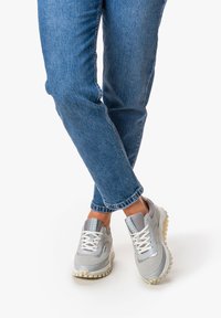 Scarpe sportive grigie in materiale mesh e sintetico, con suola spessa e lacci bianchi, abbinate a jeans in denim blu.