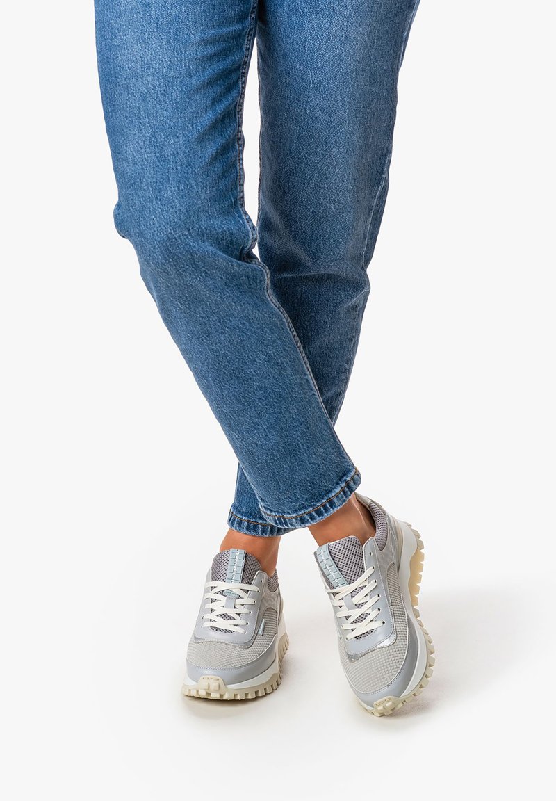 Scarpe sportive grigie in materiale mesh e sintetico, con suola spessa e lacci bianchi, abbinate a jeans in denim blu.