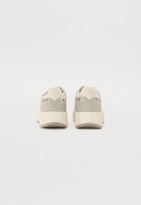 Schoenen met een grijs en crèmekleurig textiel bovenwerk, vetersluiting en een dikke crèmekleurige zool. De achterkant heeft een logo en een gladde textuur.