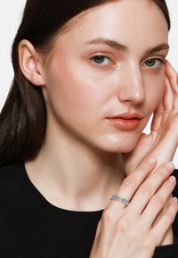 Zilveren ring met een in elkaar grijpend ontwerp, een gladde oppervlakte en een subtiele glans. De handen van het model tonen natuurlijke nagels en een minimalistische setting.