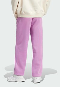 Pantalons de survêtement violets en tissu doux, avec une coupe décontractée et une taille élastique. Associés à des baskets blanches pour un look décontracté.