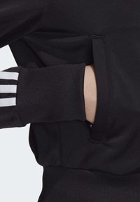 Sweatshirt noir avec une finition texturée. Présente une poche latérale avec une ouverture dissimulée et des accents rayés sur le poignet.