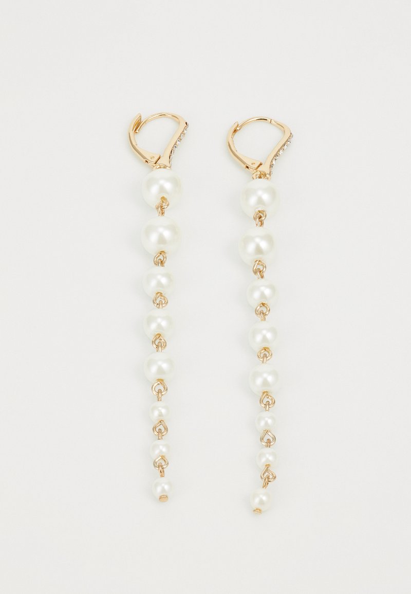 Zlato tono uhani s kljukico, ki imajo padajoče bele bisere različnih velikosti, z zunanjim povezanim dizajnom za dodano teksturo in detajle.