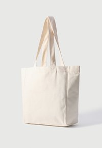 Canvas totebag i off-white. Har to lange håndtak, rektangulær form, teksturert stoff og synlige sømdetaljer.