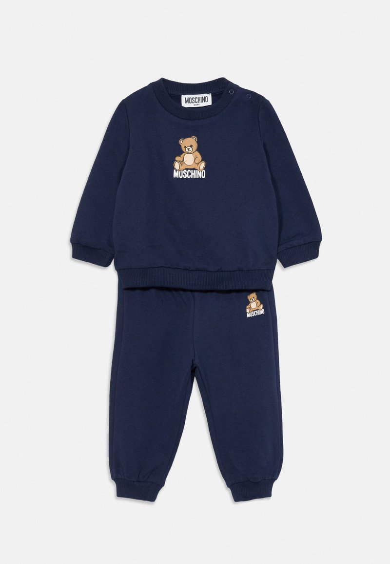 Conjunto de sweatshirt e calças para bebé em azul marinho, com gráfico de urso de peluche e a marca "Moschino" no peito e na perna da calça.