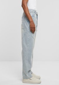 Jeans de mezclilla azul claro con un corte relajado, que presentan detalles de costura curvada y dos bolsillos laterales, combinados con zapatillas blancas.
