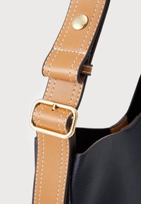 Borsa a spalla con corpo in pelle blu marina e tracolla in finta pelle color cammello. Presenta hardware dorato e cuciture bianche in contrasto per i dettagli.