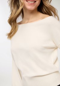 Maglione color crema chiaro con scollatura ampia, maniche lunghe e vita aderente. Tessuto morbido e design semplice, adatto per essere indossato a strati.