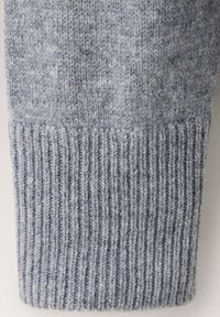 Gros plan d'une manche en tissu tricoté doux, gris clair, avec une texture côtelée au niveau du poignet et des fibres de fil fines et duveteuses.