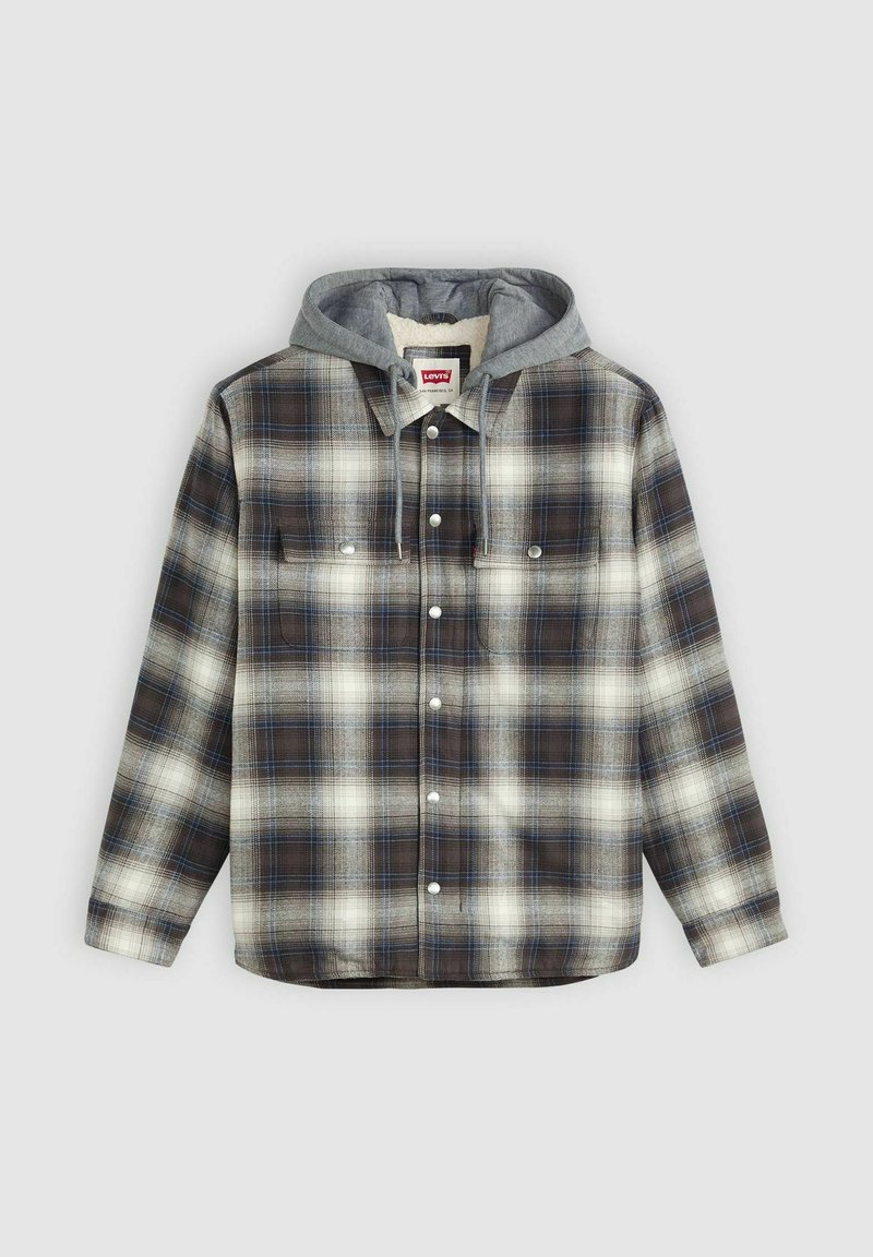 Chemise en flanelle avec capuche grise, présentant un motif à carreaux noir, blanc et bleu, deux poches poitrine et une fermeture par boutons-pression.