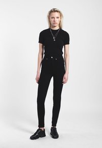 T-shirt nera e jeans skinny neri a vita alta, abbinati a sneakers nere lucide. Vestibilità slim con dettagli minimi e un leggero lucido.