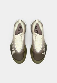 Sneakers Lacoste με γραδίαντ σχέδιο από κρέμα σε καφέ, με υφασμάτινο πλέγμα, λευκές κορδόνες και πράσινη καουτσούκ σόλα.