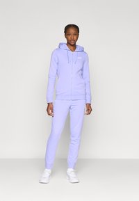 Μωβ φούτερ με φερμουάρ και μπροστινή τσέπη, συνοδευόμενο από ταιριαστό παντελόνι jogging. Μαλακό υλικό, ελαστικές μανσέτες και κορδόνια, με διακριτικό λογότυπο στο στήθος.