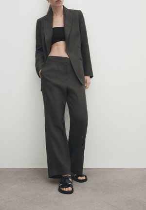 Ciemnozielony marynarka dopasowana, zestawiona z czarnym krótkim topem, spodniami typu wide-leg oraz czarnymi sandałami na paski. Gładki materiał o sztywnej formie.