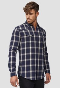 Navy and white plaid long-sleeve shirt made of a soft fabric, featuring two chest pockets and button closure, with a tailored fit.