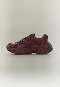 Μαρόν αθλητικό παπούτσι με χοντρή σόλα, επάνω μέρος από δίχτυ και δέρμα, περίτεχνη ραφή και κλείσιμο με κορδόνια, εμφανιζόμενο σε πλευρική προβολή σε απλό φόντο.