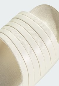 Slide sandal in off-white, featuring a textured upper with multiple horizontal grooves and a smooth, curved footbed.