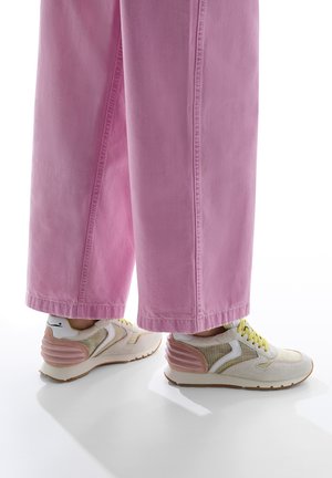 White and pink athletic sneakers with a netted texture and yellow laces, paired with loose pink denim pants, showcasing wide legs.