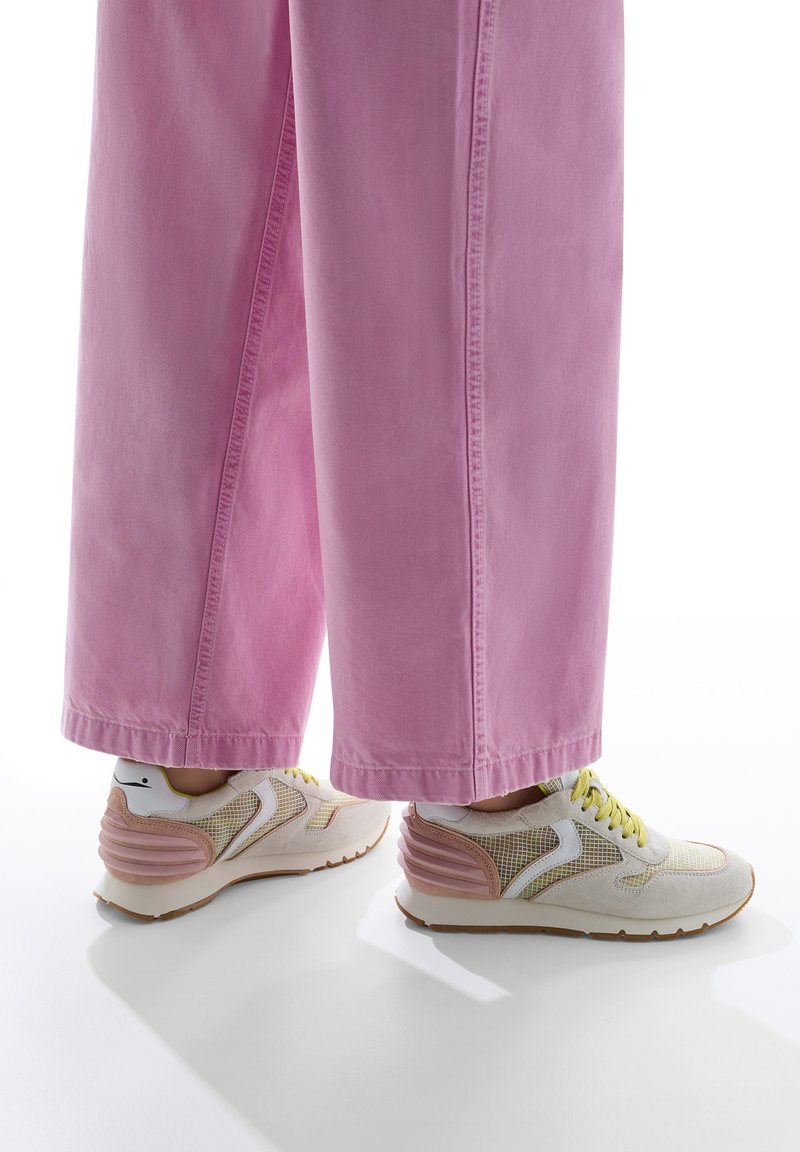 Weiße und rosa Sport Sneaker mit einer netzartigen Textur und gelben Schnürsenkeln, kombiniert mit lockeren rosafarbenen Jeanshosen mit weiter Schnittform.