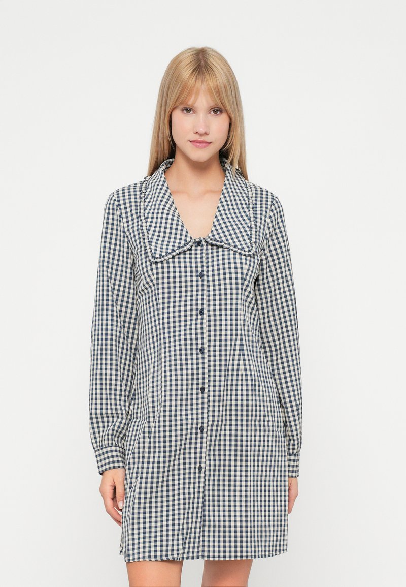 Φορεματίτσα με κουμπιά σε ναυτικό και κρεμ καρό σχέδιο, διαθέτοντας μακριά μανίκια, μεγάλο γιακά και πλάγιες τσέπες.