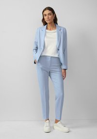 Svetle modrý oblekový blazer a odpovídající kalhoty, vyrobené z hladkého materiálu, doplněné bílým topem a bílými platformovými teniskami.