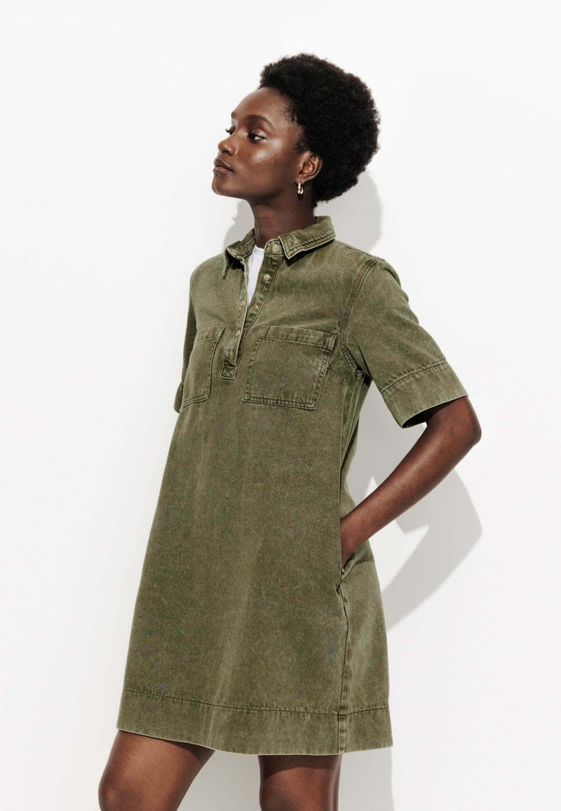 Robe à manches courtes, couleur vert kaki, en tissu doux, avec un col, une patte de boutonnage et deux poches avant.