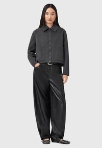 Veste en laine grise coupée avec une fermeture éclair, deux poches avant, associée à un pantalon large en cuir noir et des chaussures noires à motif.