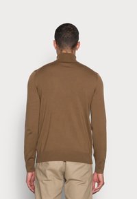 Brun, ribbstickad turtlenecktröja bärs med beiga byxor. Har långa ärmar, en figurnära silhuett och en subtil struktur.