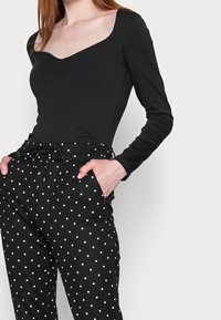 Svart långärmad bodysuit med fyrkantig halsringning, kombinerad med högmidjade svarta byxor med vita prickar och dragsko i midjan.