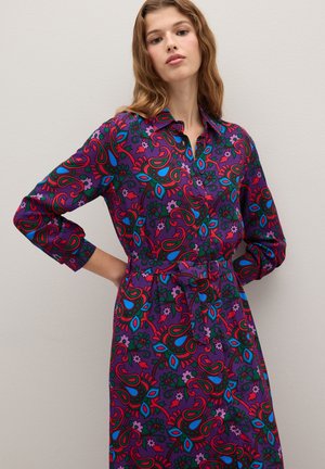 Robe à motifs en violet, ornée de dessins floraux rouges, bleus et verts. Devant boutonné avec une taille nouée et des manches longues. Texture de tissu lisse.