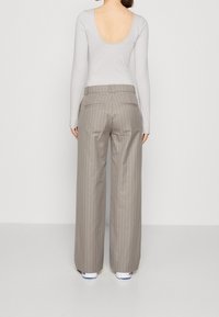 Beige gestreepte wijde broek met een ceintuur en achterzakken, gecombineerd met een lichtgrijze lange mouw top met een lage rug.