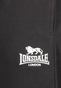 Black sweatpants made from cotton, featuring a white embroidered logo of a lion and the text "LONSDALE LONDON" on the left side.