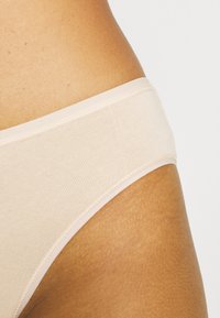Beige bomullsunderbukser med en jevn, ribbet tekstur og en myk elastisk midjebånd, med rene sømmer og et minimalistisk design.