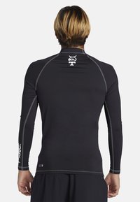 Černá dlouhá tričko s dlouhým rukávem vyrobené z elastické látky, s malým bílým logem na zadní straně a šedými kontrastními stehy podél švů.