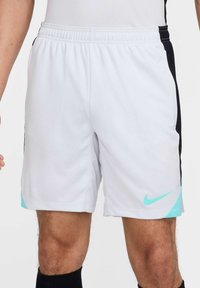 Witte sportshorts met zwarte zijpanelen, een elastische tailleband en turquoise Nike-logo accenten aan de zoom. Gemaakt van lichtgewicht materiaal.