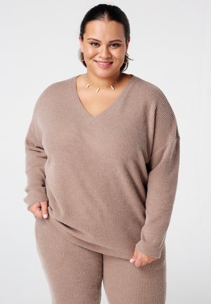 Pull en maille côtelée beige avec un col en V, des manches longues et une coupe décontractée, assorti à un pantalon en maille côtelée. Texture lisse sur l'ensemble.