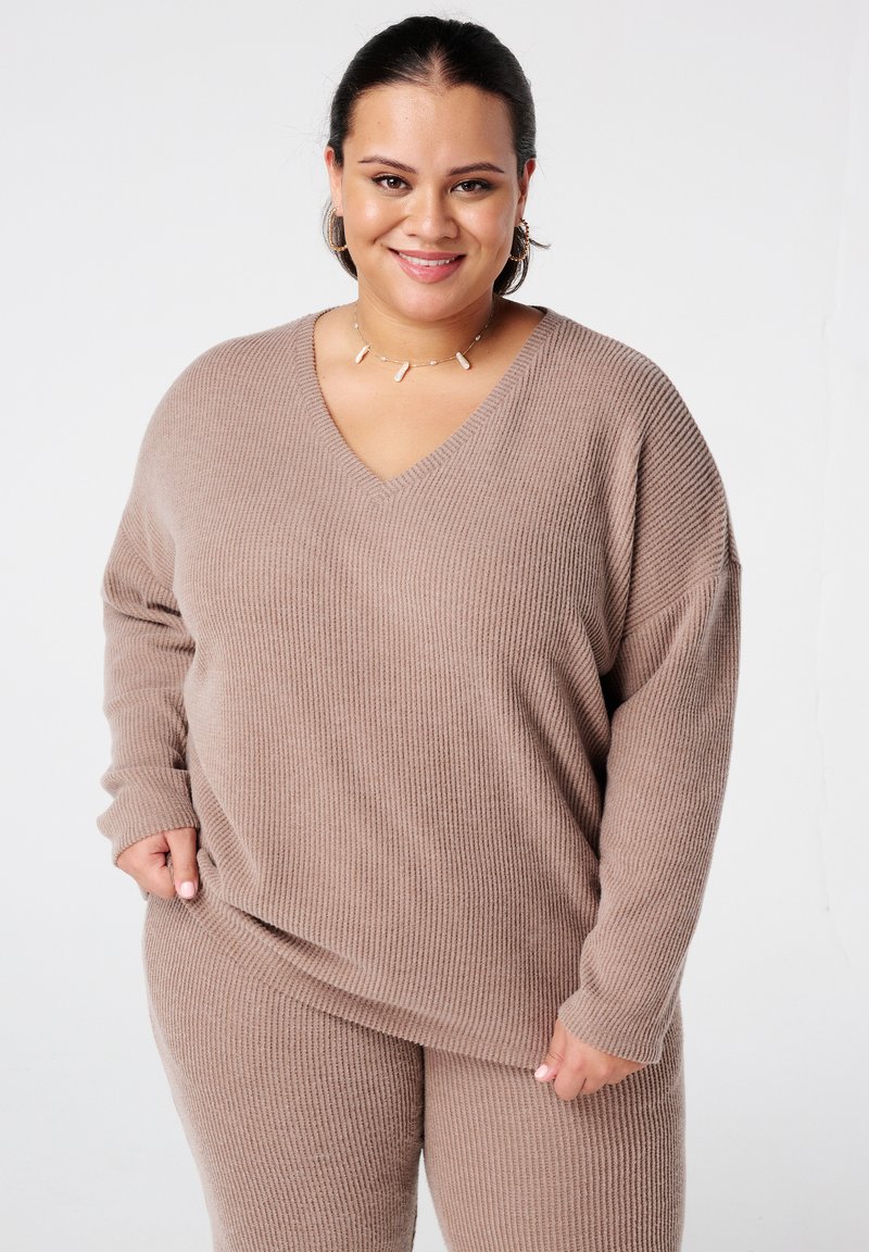 Pull en maille côtelée beige avec un col en V, des manches longues et une coupe décontractée, assorti à un pantalon en maille côtelée. Texture lisse sur l'ensemble.